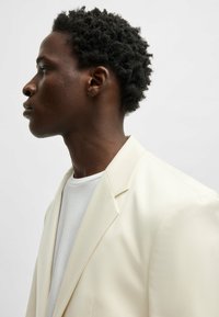 White blazer with a textured finish featuring notched lapels, paired with a white crew neck t-shirt, viewed from the side.
