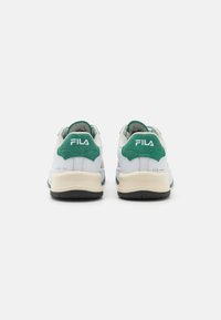 Sneakers FILA bianchi e verdi mostrati da dietro, con suole intermedie color crema e suole nere su uno sfondo chiaro e semplice.
