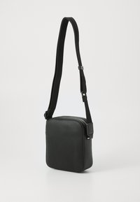 Borsa a tracolla nera con forma quadrata, superficie texturizzata, tracolla regolabile e chiusura a zip. Il materiale sembra essere sintetico.