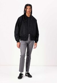 Chaqueta bomber negra con puños acanalados, combinada con pantalones gris ajustados y zapatillas negras con franjas blancas. Estilo casual y urbano.