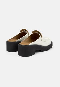 Scarpe slip-on bianche con punta tonda, dettagli marroni e una spessa suola nera a piattaforma con superficie texturizzata.