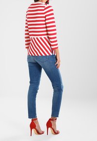 Rot-weiß gestreiftes Langarmoberteil mit einem Peplum-Design, kombiniert mit enganliegenden blauen Jeans und roten High-Heels.