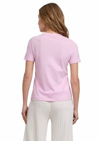 Kurzes pinkes Baumwoll-T-Shirt mit Rundhalsausschnitt und kurzen Ärmeln, von hinten betrachtet, kombiniert mit hoch taillierten, strukturierten weißen Hosen.