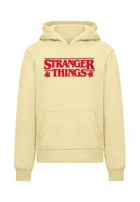 Gul huva tröja med en framficka och röd "STRANGER THINGS" text med gröna vinrankor och röda blommor som accentuerar logotypen.