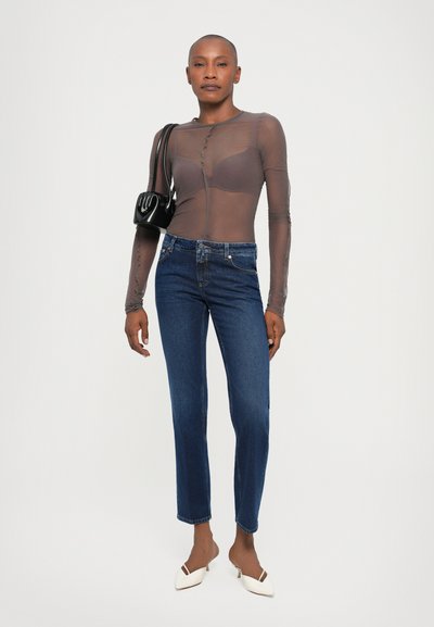Sheer gray long-sleeve top with button details, paired with blue straight-leg jeans and white heeled mules. Small black handbag included.