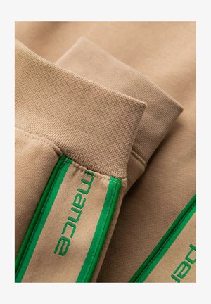 Felpa color marrone chiaro con dettagli verde sui polsini. Presenta un tessuto a maglia testurizzata e un marchio ricamato lungo il lato.