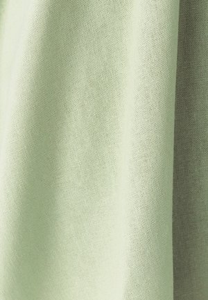 Tissu tissé vert clair avec une texture visible et de doux plis créant des ombres et des reflets.