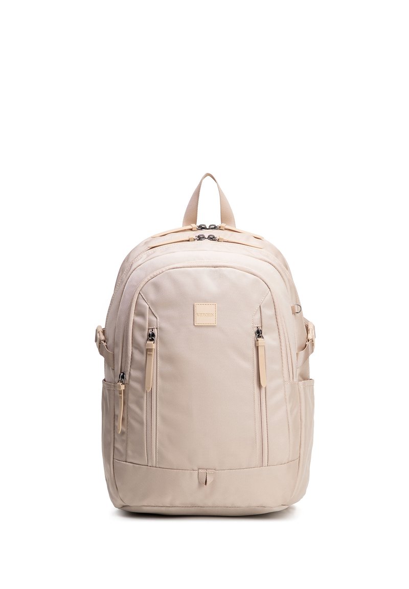 Béžový batoh s několika přihrádkami na zip, bočními kapsami, polstrovanými ramenními popruhy a horním úchytem, stojící vzpřímeně na bílém pozadí.