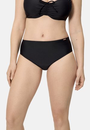 Mujer con braguitas de bikini negras de talle alto y un top de bikini a juego con un detalle de nudo en el frente, de pie frente a un fondo liso.