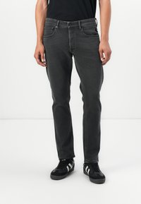 Grey denim jeans with a slim fit, featuring five-pocket design, belt loops, and a zip fly with button closure. Worn with black sneakers.