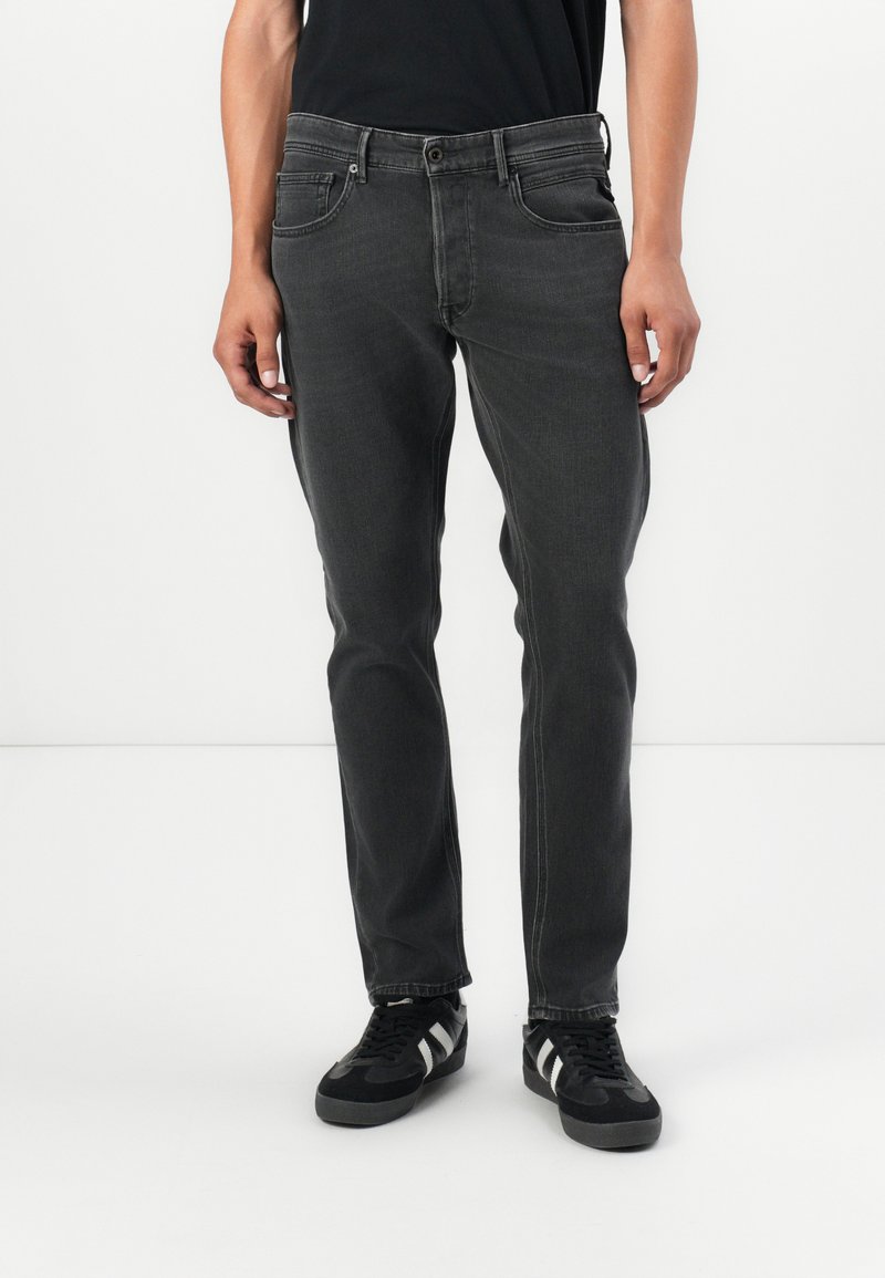 Grey denim jeans with a slim fit, featuring five-pocket design, belt loops, and a zip fly with button closure. Worn with black sneakers.
