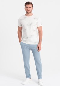 Weißes Kurzarm-T-Shirt mit verstreuten dunklen Sprenkeln, kombiniert mit hellblauen schmalen Hosen und weißen Sneakern. Einfaches, modernes Design.