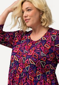 Buntes Kleid mit geometrischen Mustern in den Farben Pink, Rot und Lila, hergestellt aus einem weichen, dehnbaren Stoff mit Rundhalsausschnitt.