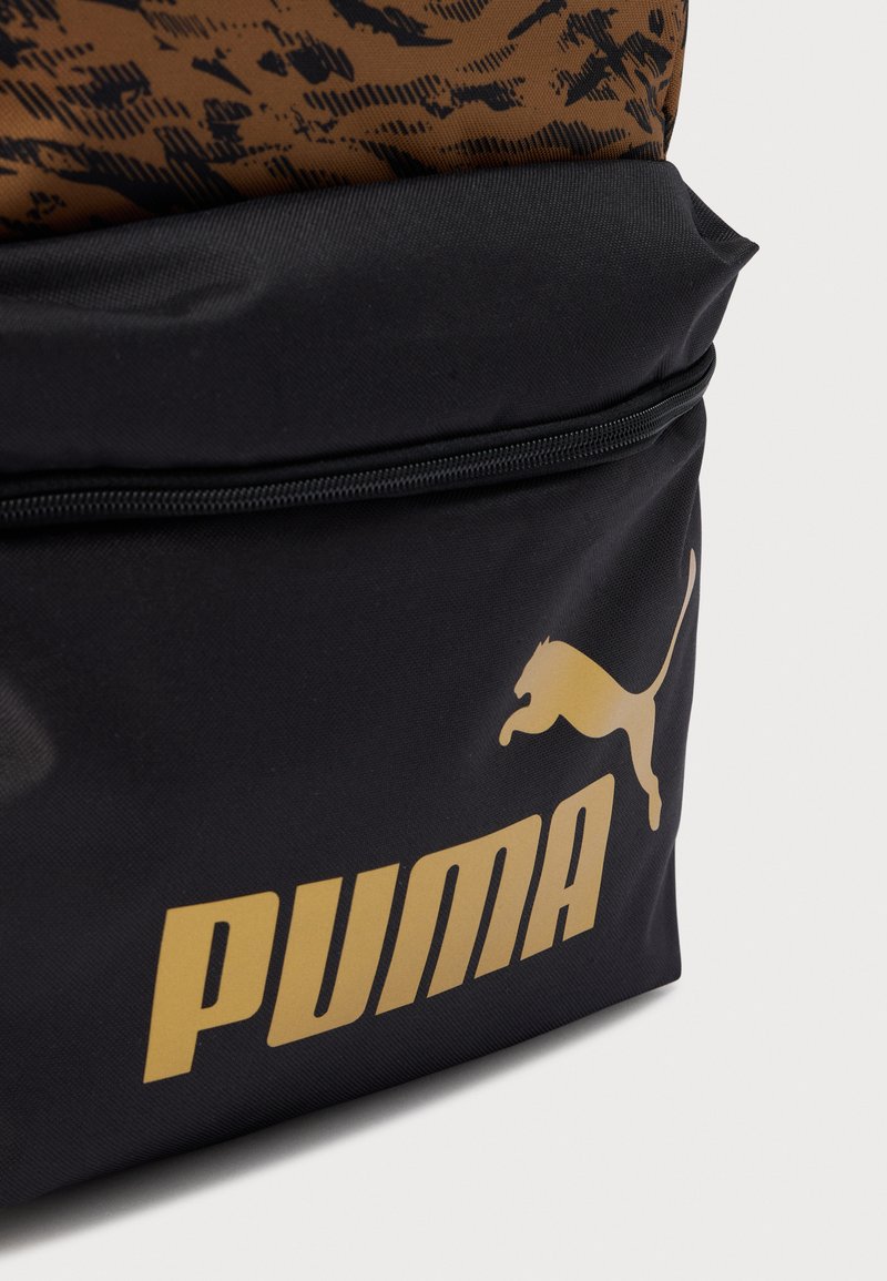 Base de sac à dos noire avec un dessus marron à motif, présentant un logo "PUMA" doré et un graphisme de puma en saut. Fermeture éclair visible.