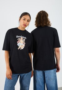 Svart oversized t-skjorte med et sentralt fargerikt grafisk trykk av en cherub, korte ermer, ribbet rund hals og avslappet passform.