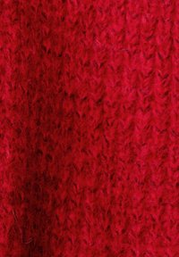 Roter gestrickter Stoff mit strukturiertem Muster, der weiche Fasern und unterschiedliche Maschen für zusätzliche Tiefe aufweist.