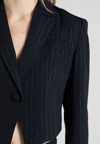 Blazer blu navy tagliato con righe argento e paillettes, dotato di colletto a scollatura e chiusura con un bottone. Tessuto morbido.
