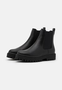 Black Chelsea boots made of smooth leather, featuring elastic side panels, pull tabs, and rugged, notched rubber soles.