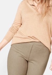 Maglione beige con colletto e maniche lunghe abbinato a pantaloni marroni a scacchi con una vestibilità aderente e tessuto testurizzato.