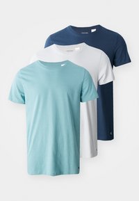 Three crew-neck T-shirts in teal, white, and navy. Soft cotton fabric with short sleeves and a modest fit. Calvin Klein logo on the hem.
