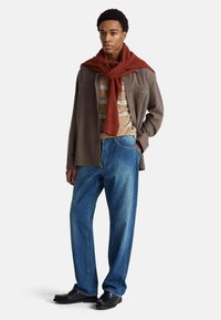 Casualny strój składający się z brązowej koszuli na guziki, paskowanej koszulki w kolorze beżowo-niebieskim, czerwonego wełnianego szalika, luźnych niebieskich dżinsów i czarnych butów.