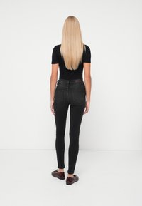 Jeans skinny negre cu talie înaltă, dotate cu buzunare pe spate și o textură netedă, purtate cu pantofi slip-on negri și un top negru ajustat.