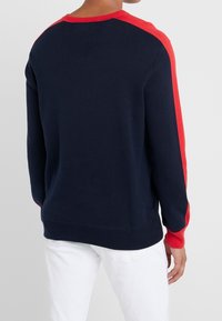 Navy sweatshirt with red shoulder accents, crew neck, and ribbed cuffs, made of soft knit material. Simple, sporty design.