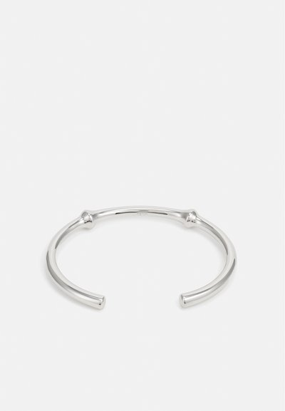 Bracciale in argento con un design liscio e arrotondato, caratterizzato da estremità aperte e piccoli accenti sferici su ciascun lato.