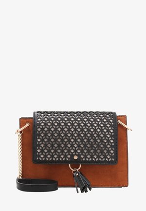 Prostokątna torba na ramię z brązowego zamszu z czarną klapą z geometrycznym wycięciem, złotym łańcuszkiem i czarnym chwostem zwisającym z przedniego zapięcia.