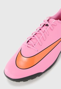 Rozā sporta kurpe ar melnu un oranžu Nike swoosh, ar gludu sintētisku virsu un plakaniem lencēm. Gumijas zole ar teksturētu saķeri.
