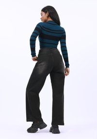 Jeans de pierna ancha negros combinados con una camiseta de manga larga a rayas en negro y azul verdoso, que muestra un diseño ajustado y una textura de punto. Zapatillas negras.