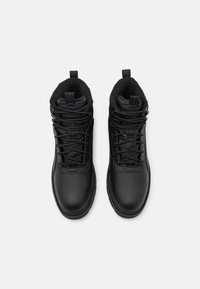 Bottines noires en synthétique avec une texture lisse, dotées d'un col rembourré, d'un laçage et de tirants pour un enfilage facile.