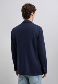 Blazer azul marino con cuello estructurado, diseño de un solo botón y puños abotonados, fabricado con un tejido texturizado. Vista trasera.