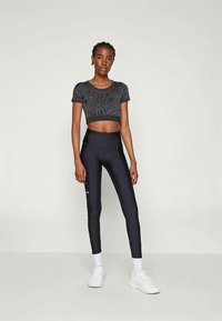 Czarny top w wzory z krótkimi rękawami, zestawiony z legginsami w kolorze granatowym o wysokim stanie, noszony z białymi trampkami i skarpetkami do kostek.