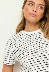 Vit bomull T-shirt med svarta vågiga randmönster, korta ärmar och rundad halsringning. Slät textur.