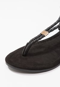 Black flip-flop featuring woven black straps and gold hardware accents. The sole is made of soft, textured material for comfort.