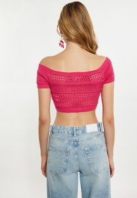 Růžový pletený crop top bez ramínek s texturovaným vzorem, spárovaný s vysokými světle modrými džíny s zadními kapsami.
