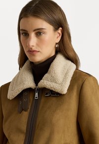 Giacca in suede marrone con colletto in shearling beige, caratterizzata da una chiusura a zip, dettagli in pelle e accessori in metallo.