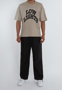 Camiseta de manga corta color beige con letras en negro que dicen "LOW LIGHTS" y un diseño gráfico. Combinada con pantalones negros de corte holgado y zapatillas blancas.