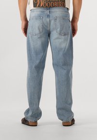 Ljusblå denimjeans med avslappnad passform, fem fickor och en urtvättad texture. Bärs med en beige grafisk t-shirt och mörka slip-on skor.