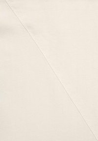 Béžová látka s texturovaným povrchem, s diagonálním švem, který vytváří subtilní grafický prvek proti hladkému materiálu.