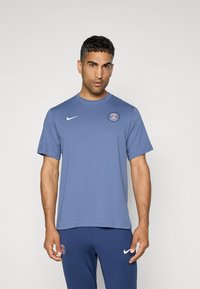Blå bomulds T-shirt med rund hals, korte ærmer og et logo på brystet. Sættes sammen med marineblå bukser med et lignende logo.