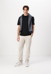 Svart t-skjorte, beige cargo-bukser og hvite sneakers. Blå hettegenser drapert rundt halsen med glidelås og kontrasterende hvit kant. Glatt tekstur.