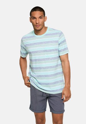 Hombre con camisa de manga corta de rayas azul claro y gris con un bolsillo en el pecho y pantalones cortos gris oscuro remangados.