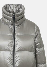 Zilveren pufferjack met hoge kraag, voorrits en geborduurd patroon. Het materiaal heeft een glanzende afwerking en gevoerde secties.