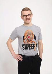 Šedé bavlněné tričko s grafikou plyšového psa s hravým výrazem a slovy "SWEEP!" tučně napsanými pod ním.