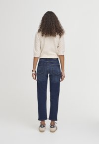 Suéter de punto beige claro con mangas texturizadas, combinado con jeans de pierna recta azul oscuro y zapatillas beige con acentos negros.