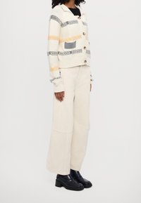 Sweter robiony na drutach z kremowym tłem, czarnymi i żółtymi poziomymi paskami, z przodu na guziki i naszywaną kieszonką. Połączony z beżowymi spodniami o szerokich nogawkach i szpilkami.