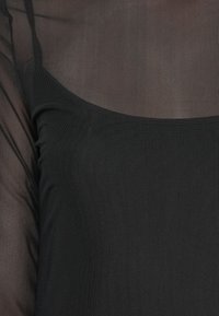 Top nero trasparente con una texture morbida, dal design aderente senza maniche e con scollatura rotonda, che consente di vedere i capi sottostanti.