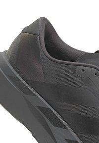 Κοντινή λήψη της φτέρνας ενός μαύρου αθλητικού παπουτσιού με υφασμάτινη υφή, επενδυμένο κολάρο και γεωμετρικό μοτίβο στη σόλα.